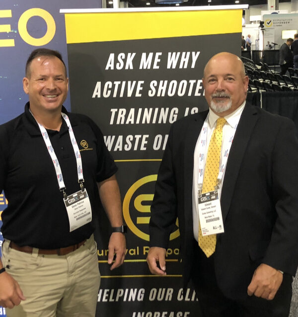 Two professionals smiling at a security conference in front of a banner about active shooter training.