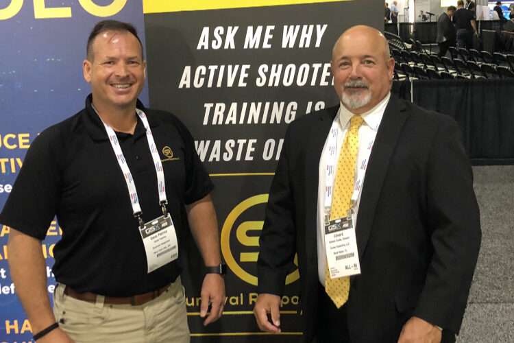 Two professionals smiling at a security conference in front of a banner about active shooter training.