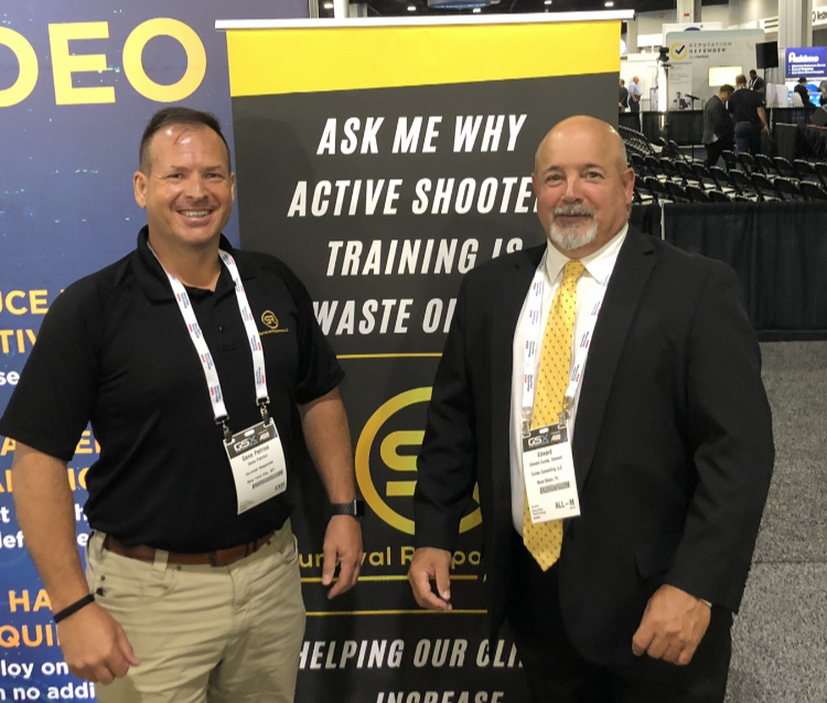 Two professionals smiling at a security conference in front of a banner about active shooter training.