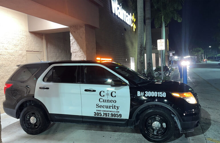 Cuneo Consulting security patrol car with flashing lights parked outside a Walmart at night.