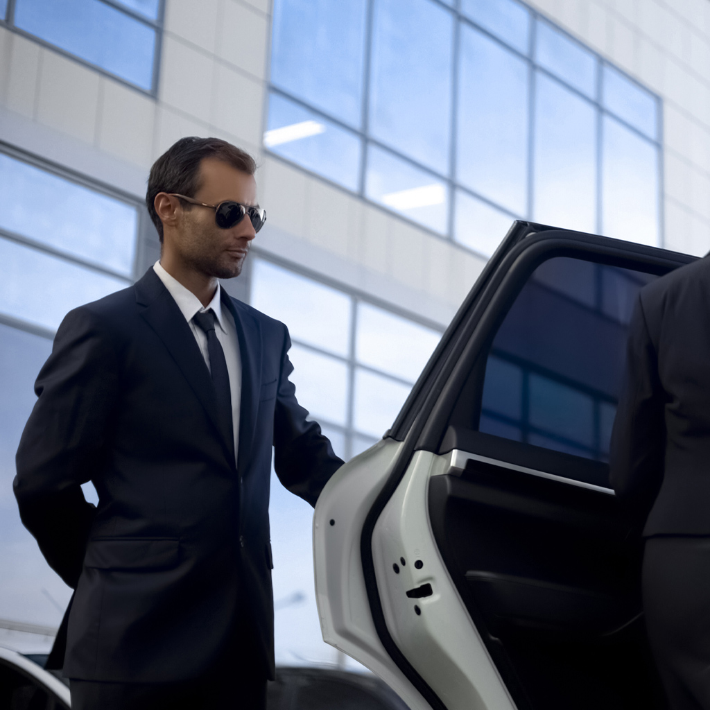 Professional security agent in a suit opening a car door, displaying vigilance and readiness