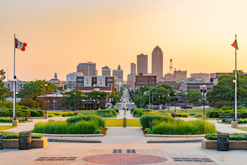 Des Moines skyline at dusk with the Iowa state flag and American flag in the foreground.