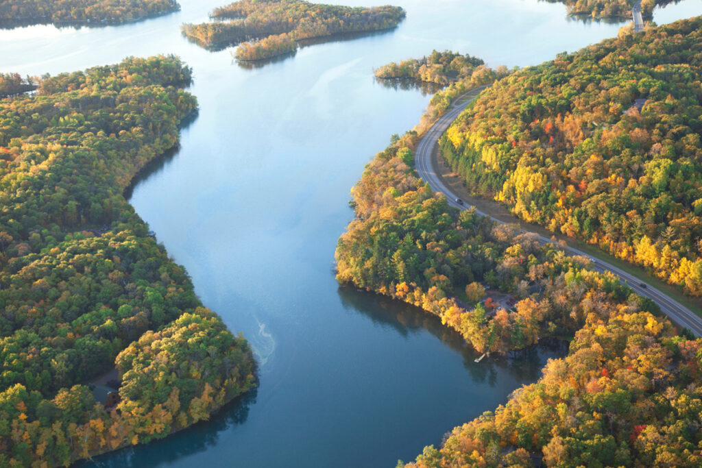 Aerial view of a meandering river flanked by a road and vibrant autumn foliage.