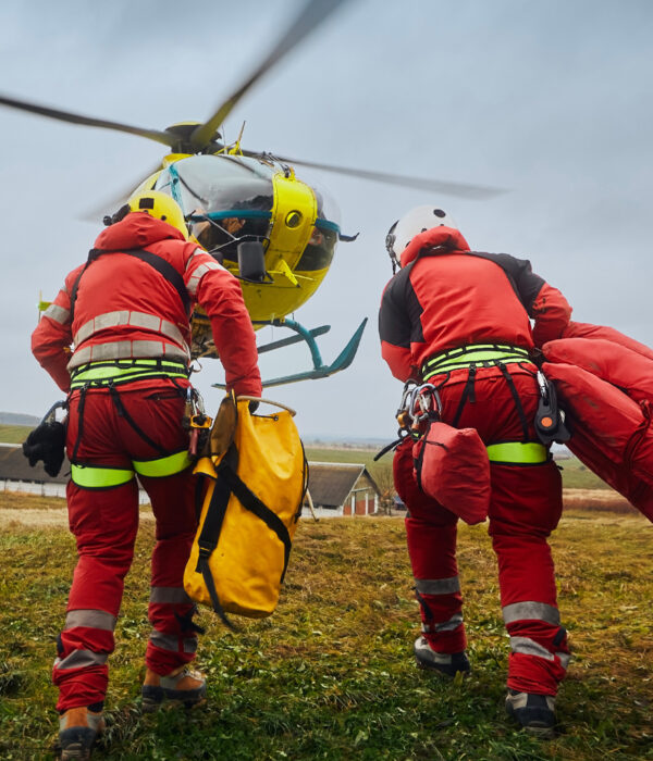 Emergency response team in red suits preparing for a helicopter mission on a grassy field.