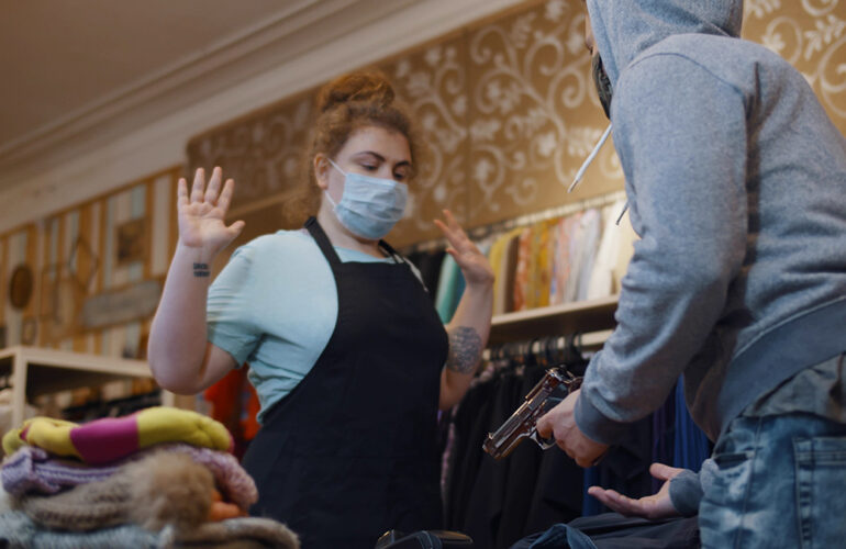 A simulated scenario in a retail store showing a staff member with raised hands facing a mock robber to depict a theft incident.