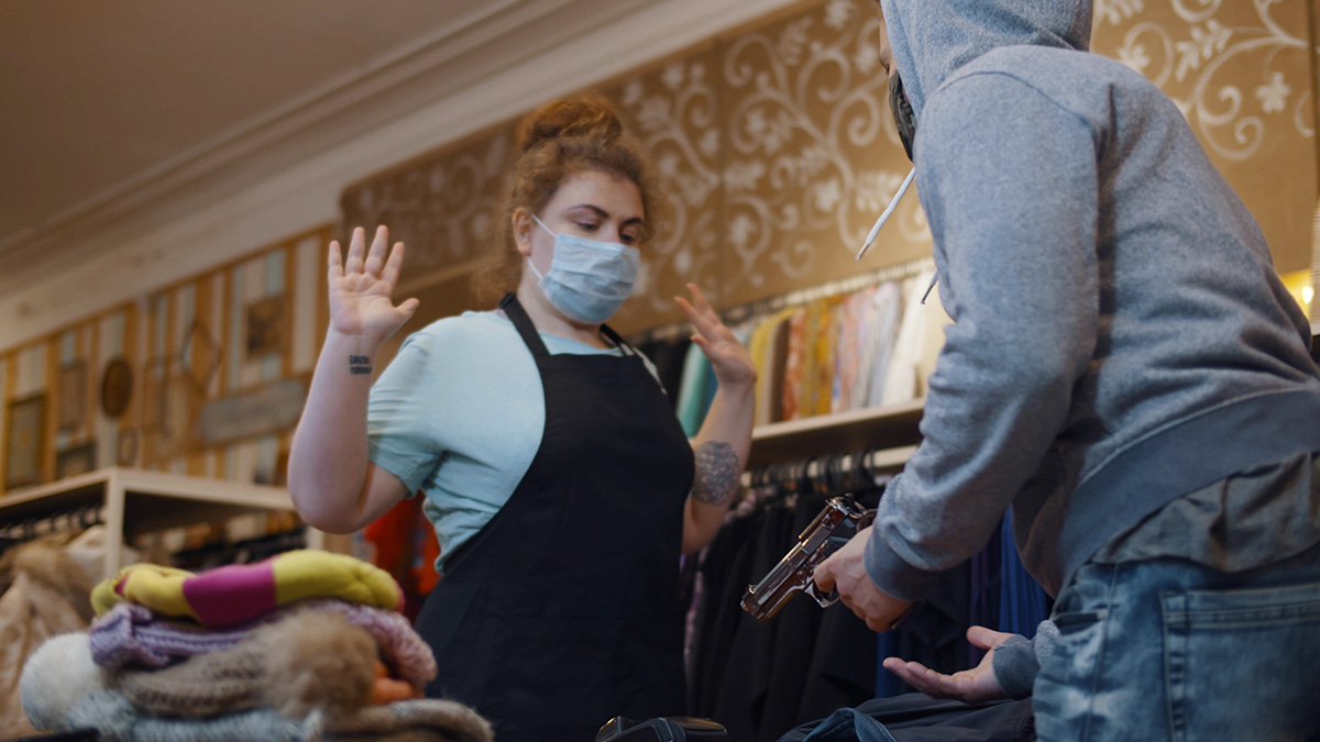 A simulated scenario in a retail store showing a staff member with raised hands facing a mock robber to depict a theft incident.